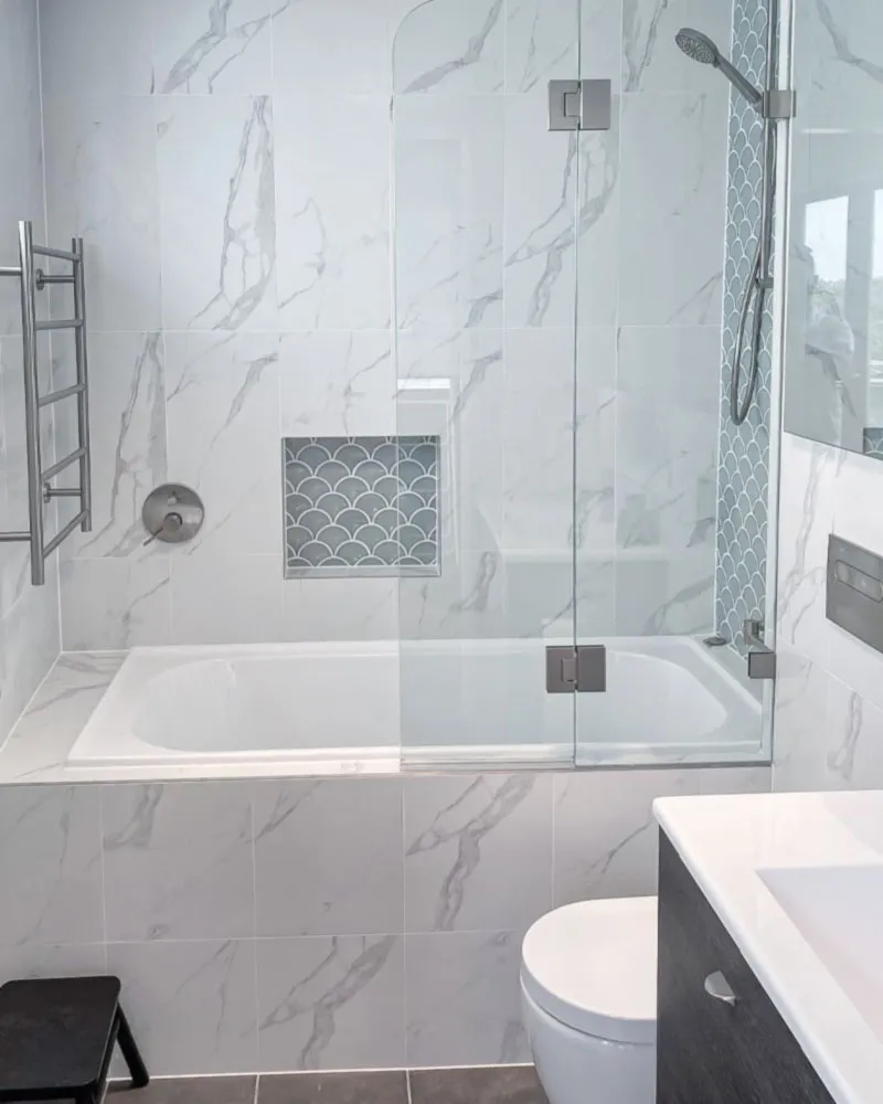 Bathroom with a shower over the bath, glass screen and marble-look wall tiles