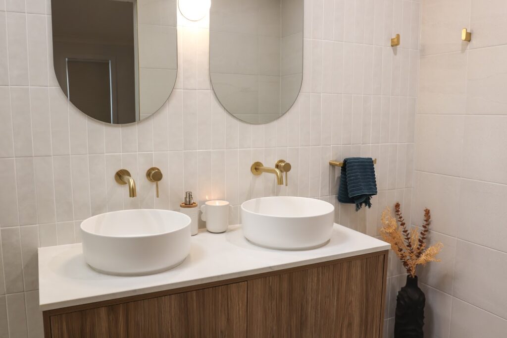 double bathroom vanity with timber cabinetry, round mirrors and brushed brass tapware